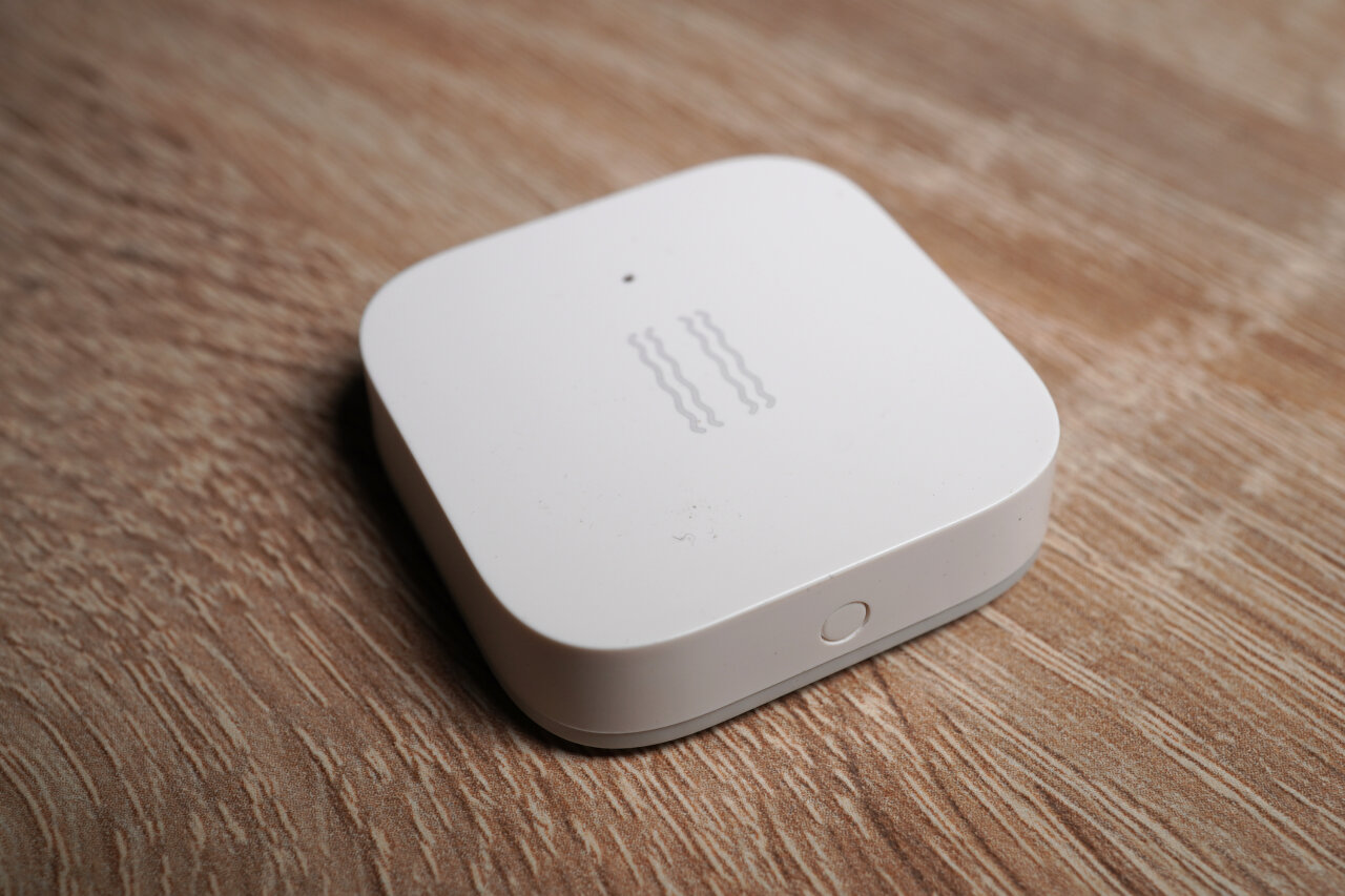 Photo of the Xiaomi Aqara Vibration sensor. A white rectangular box with a little button to connect.