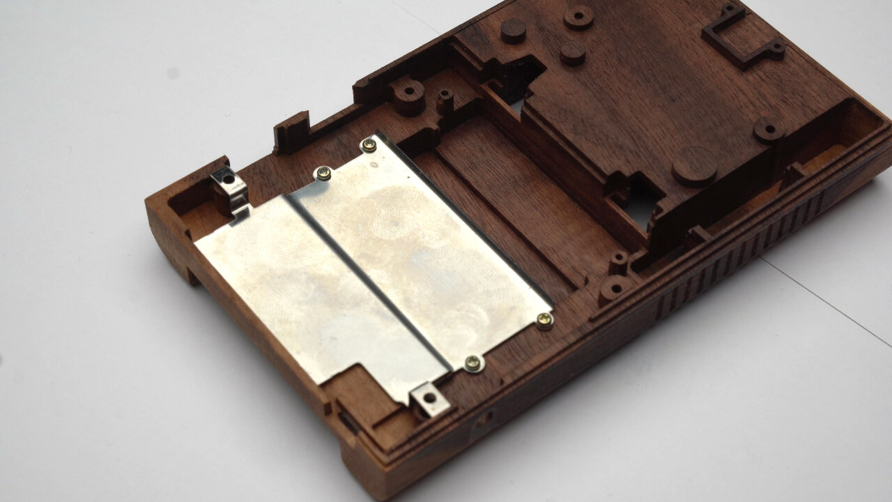 Photo of the mostly empty bottom half of the wooden Game Boy shell. A metal shield from an original Game Boy has been screwed into it.